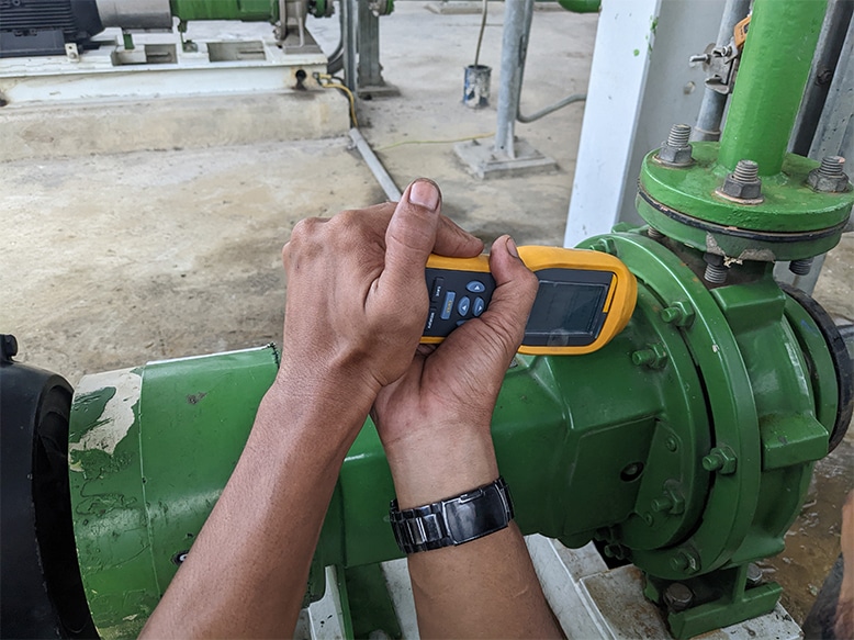 worker inspecting for cavitation damage of pump with vibration monitor