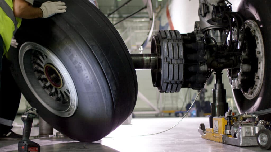 Close-up of a large aircraft wheel and engine gear on a maintenance stand, with a gloved hand resting on the tire.
