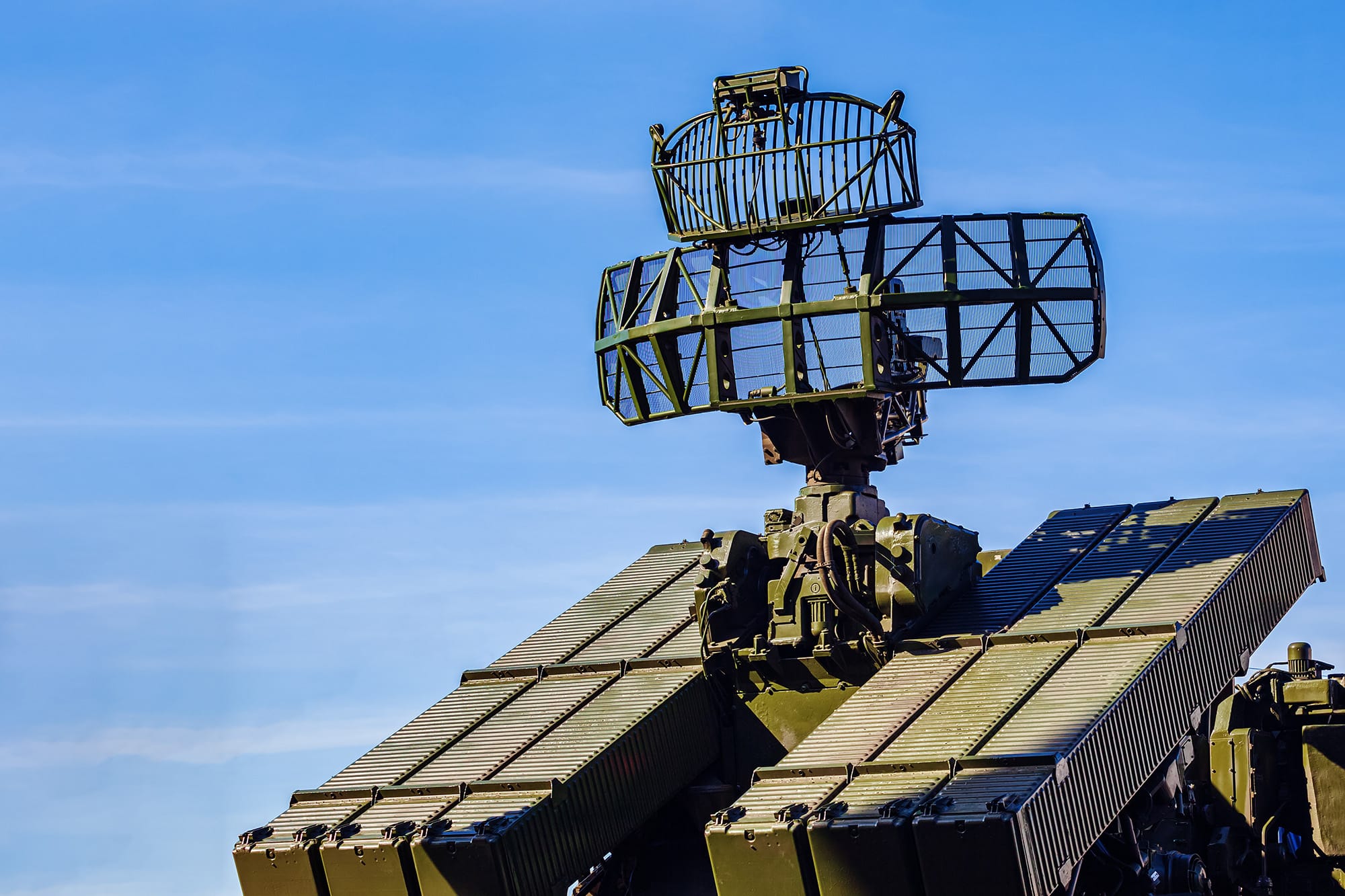 Close-up of a large olive-green military radar antenna mounted on a tracked vehicle against a clear blue sky