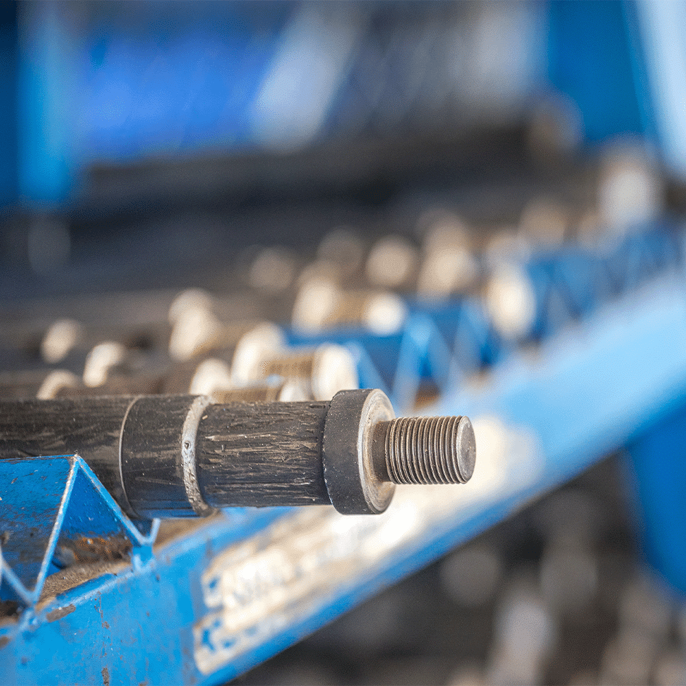 Close-up of a threaded bolt on a black rod attached to blue industrial machinery, with a blurred background of rollers.