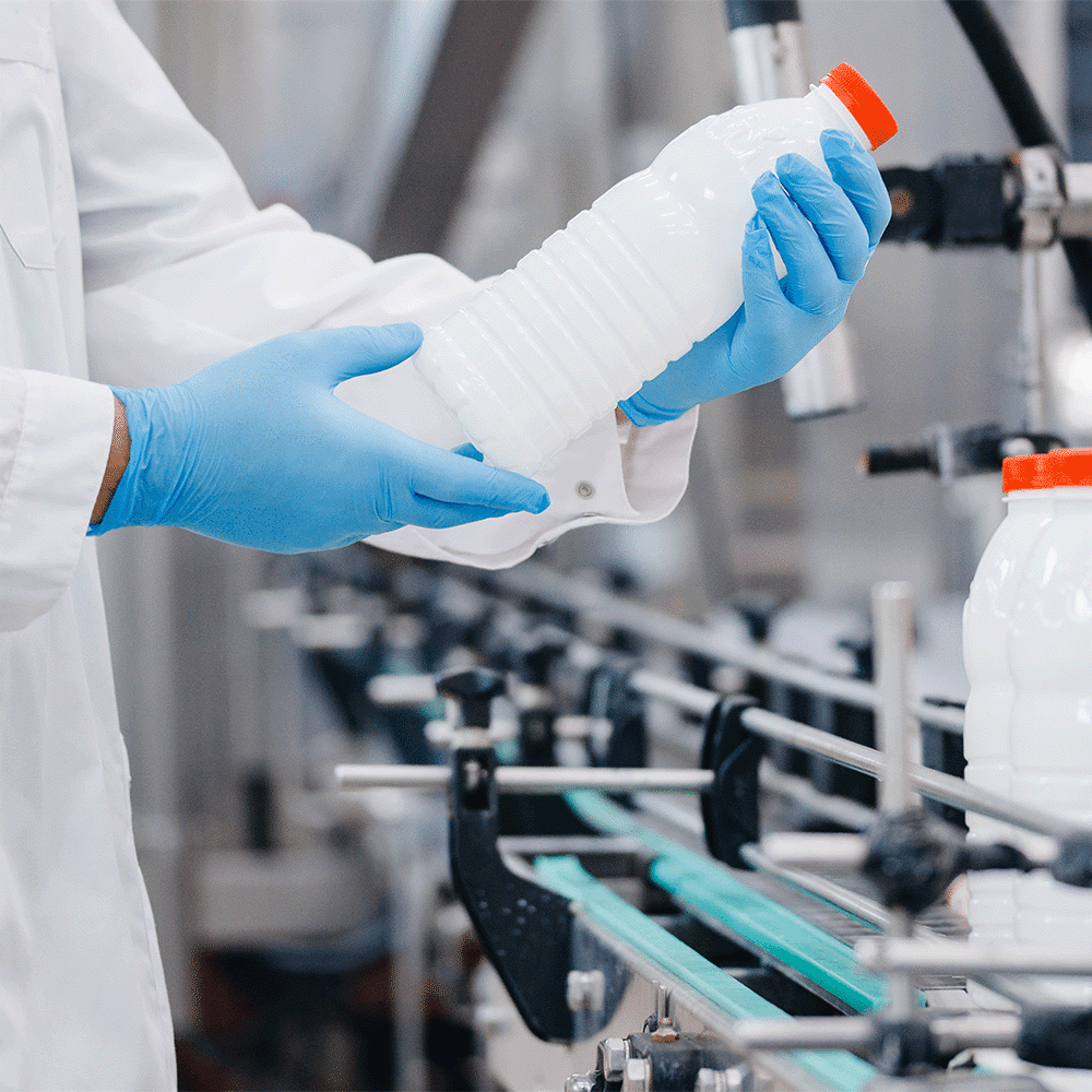 Food factory inspector examining an empty drink bottle on a food processing conveyor system, ensuring compliance with ISO 19011 audit guidelines.