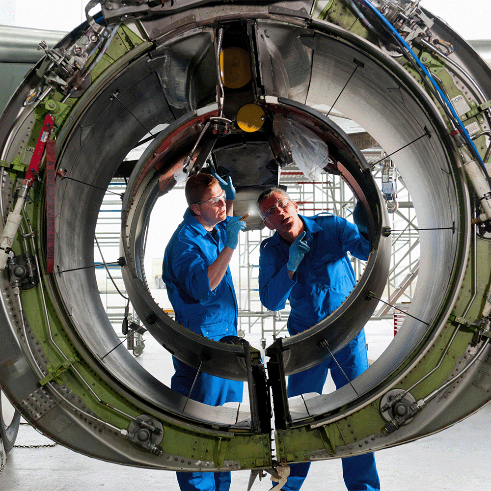 Two engineers inspect a jet engine casing to achieve AS9100D Certification for Quality Management Systems for the aerospace and defense industries.